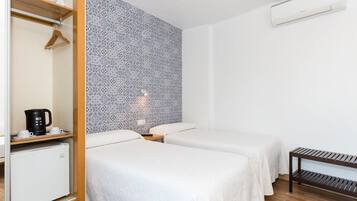 Habitación de hotel con dos camas, un armario, un refrigerador pequeño, una cafetera y un papel tapiz estampado.
