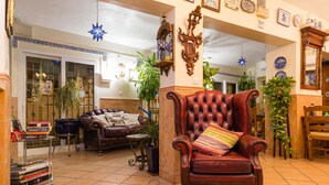 A living room with a leather armchair, a sofa, and a coffee table. There are plants, a bookshelf, and a decorative mirror. - Hostal Guadalupe (Torremolinos)
