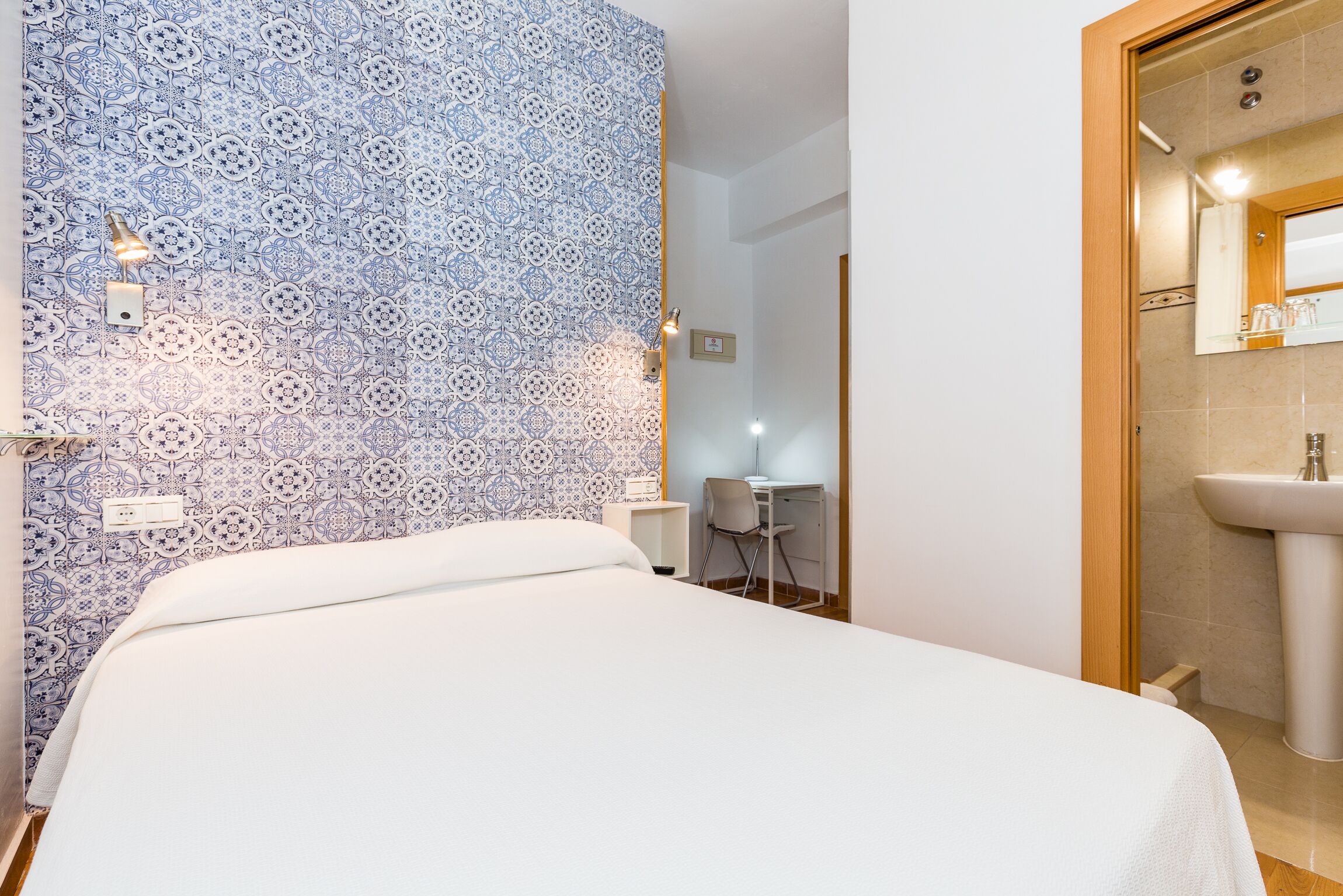 Ein Schlafzimmer mit einem Muster an der Wand, einem Bett, einem Schreibtisch und einem Badezimmer mit einem Waschbecken.