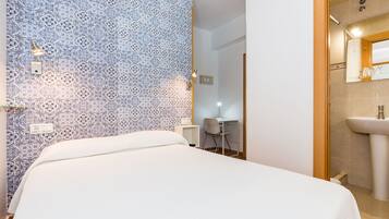 Ein Schlafzimmer mit einem Muster an der Wand, einem Bett, einem Schreibtisch und einem Badezimmer mit einem Waschbecken.