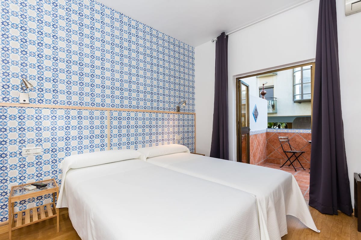 Una habitación con cama, un banco de madera y un papel tapiz estampado.