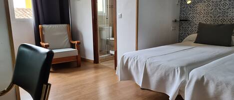 Habitación de hotel con cama, una silla y zona de ducha.