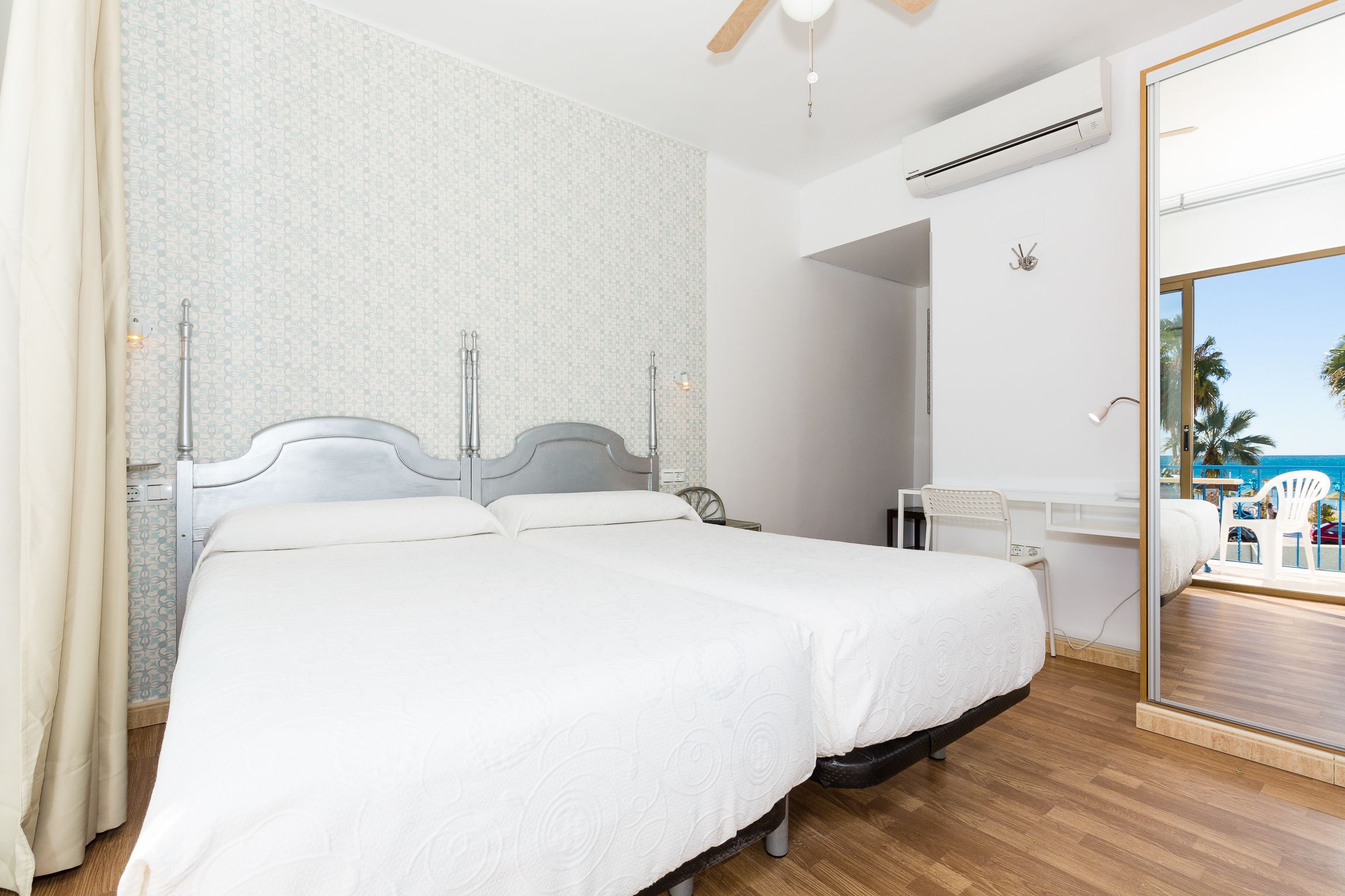 Habitación de hotel con una cama grande, un escritorio, una silla y vistas a la playa a través de un ventanal.