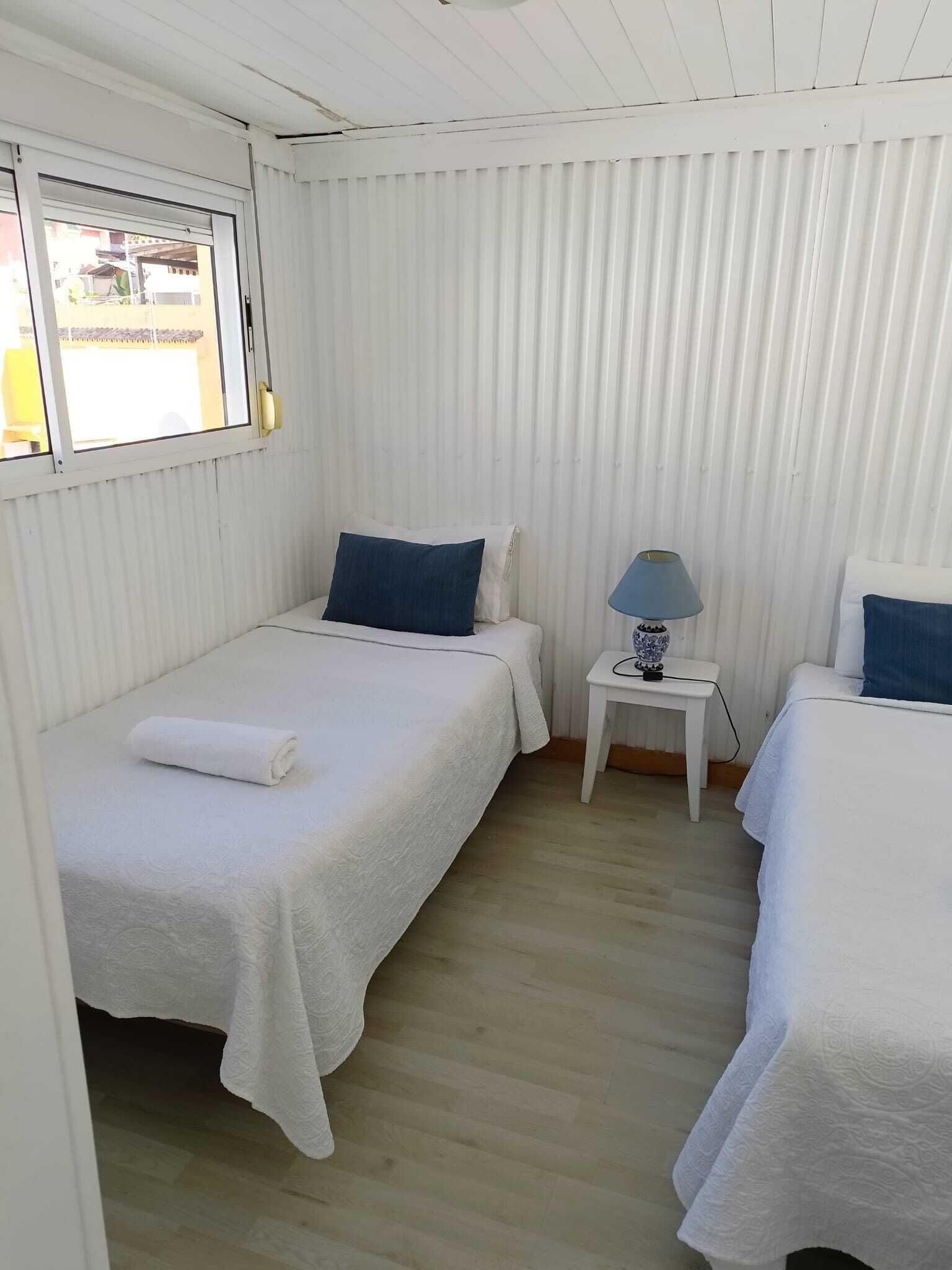 A room with two beds, a small table with a lamp, and a window.
