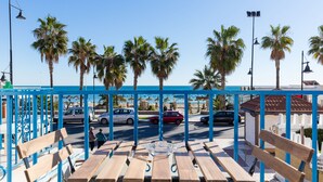 A beachside seating area with wooden benches and a clear view of the street and palm trees. - Hostal Guadalupe (Torremolinos)