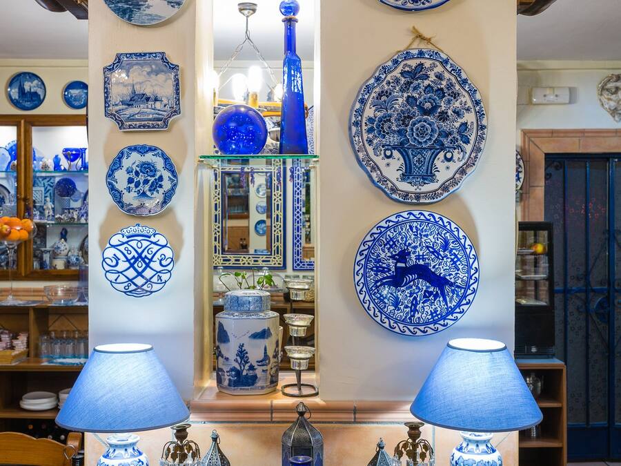 Ein Zimmer mit einem Holztisch, der verschiedene blaue und weiße Keramikstücke, darunter Teller und Vasen, sowie zwei Lampen an jeder Seite zeigt.
