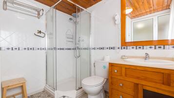 Un baño con ducha envuelta en vidrio, inodoro y armarios de madera.