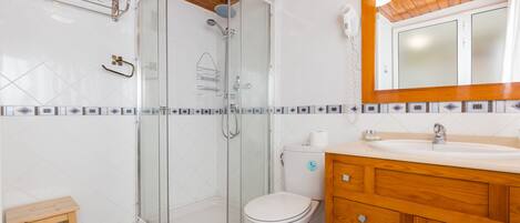 Un baño con ducha envuelta en vidrio, inodoro y armarios de madera.