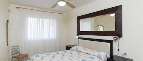 A bedroom with a bed, a chair, a nightstand, a mirror, and a ceiling fan.