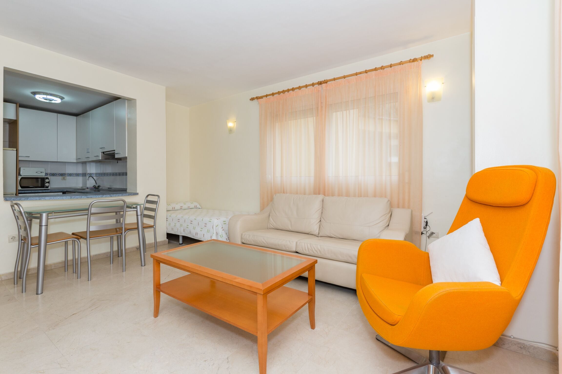A living room with a sofa, a coffee table, a dining area with chairs, and a kitchen in the background.