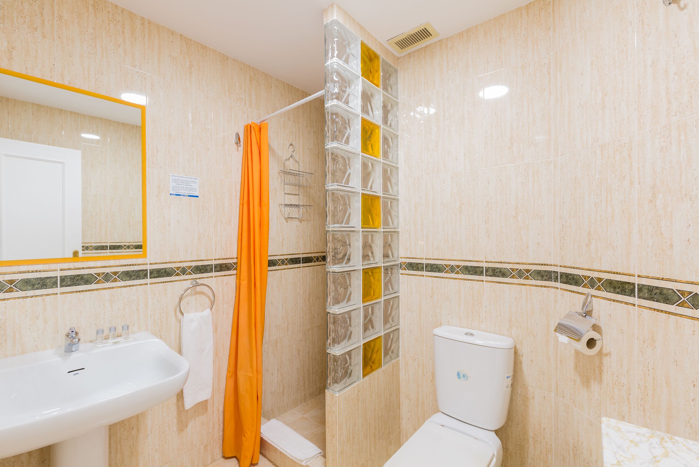 Une salle de bain équipée d’un lavabo, de toilettes, d’un rideau de douche et d’un mur en blocs de verre.