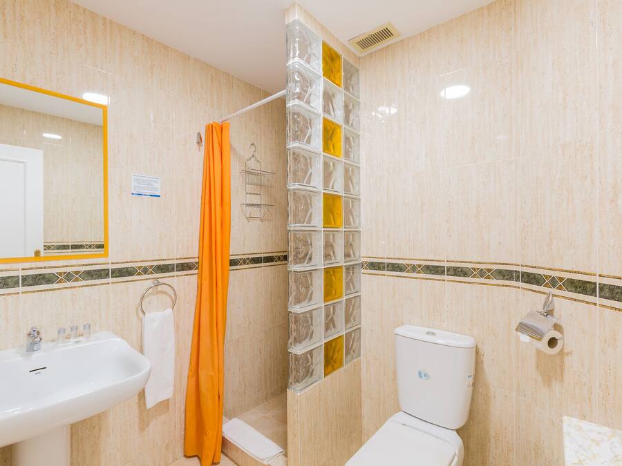 Une salle de bain équipée d’un lavabo, de toilettes, d’un rideau de douche et d’un mur en blocs de verre.
