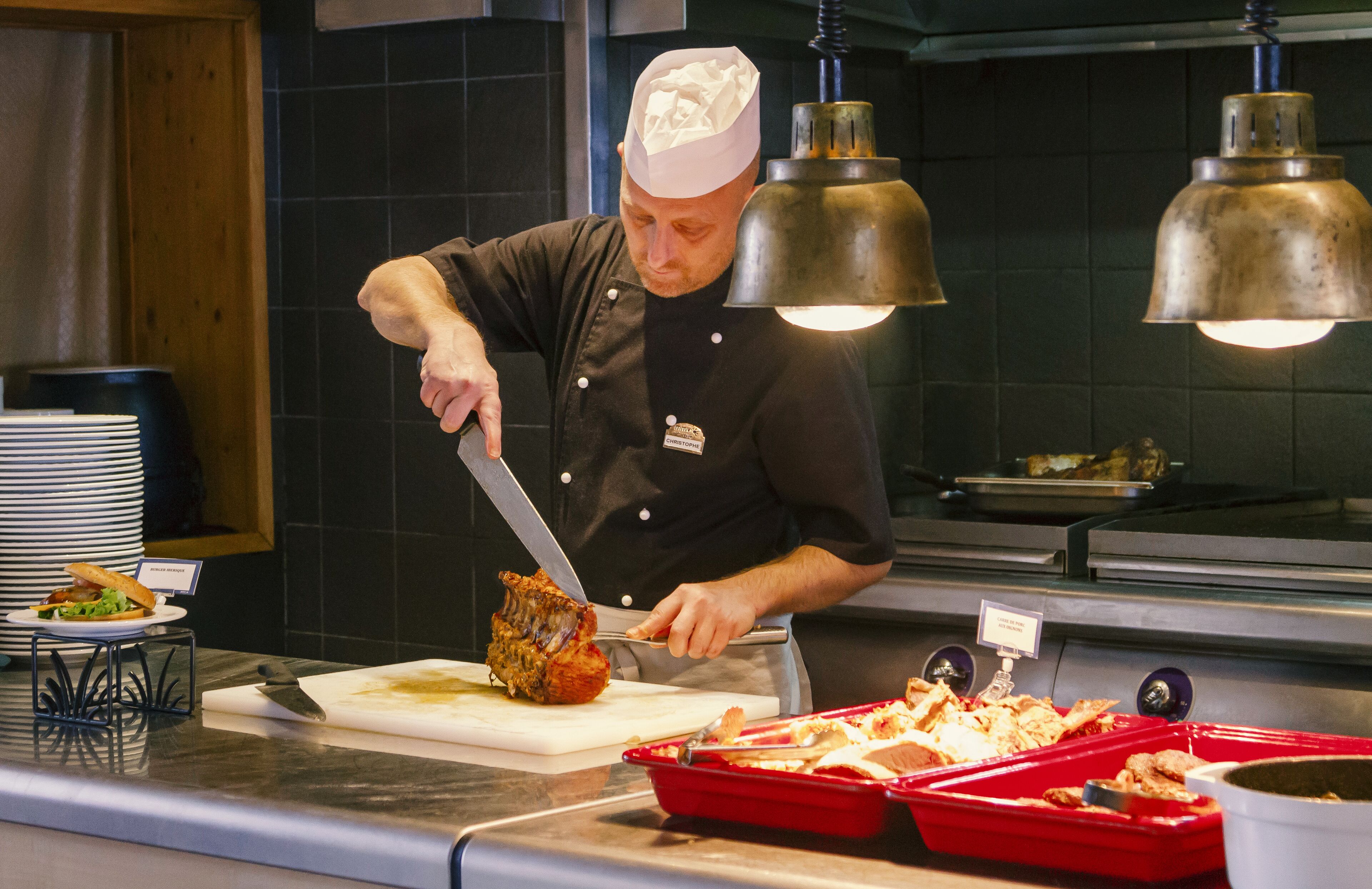 En kok skærer kød ved et buffetbord med forskellige retter og bestik.