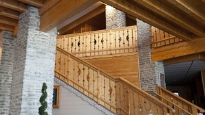 Un intérieur spacieux avec un escalier en bois, des piliers en pierre et une vue sur l’extérieur.