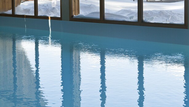 Une piscine avec vue sur un bâtiment en bois dont les toits sont recouverts de neige.
