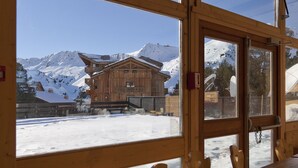 Une cabane en bois dotée de grandes fenêtres donnant sur un paysage montagneux enneigé.
