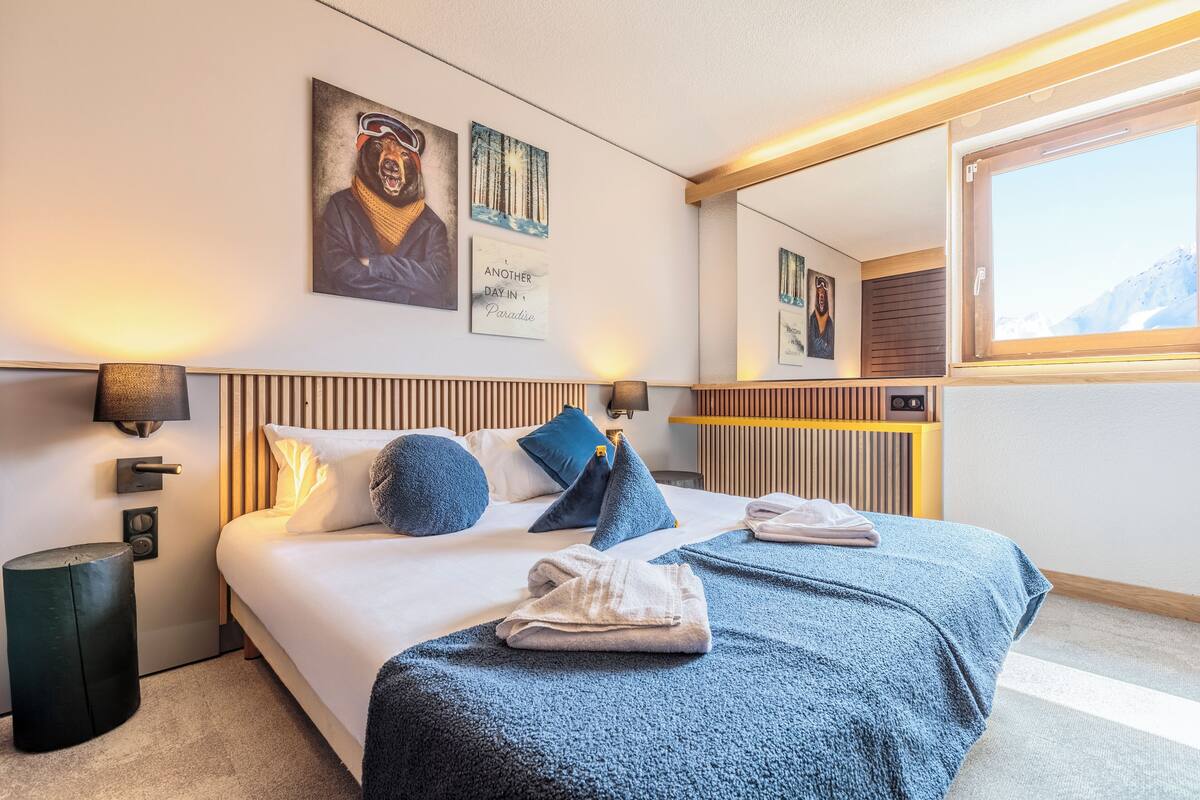 Een moderne hotelkamer met een groot bed, een houten hoofdbord, een nachtkastje, een spiegel en kunst aan de wanden.