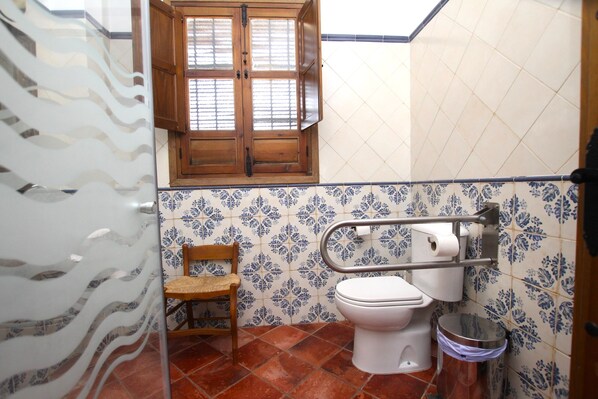 Un baño con inodoro, una silla, un ventanal y un cubo de basura.