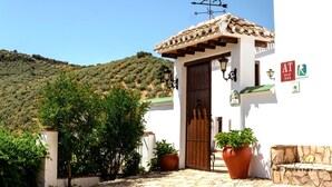 A white building with a brown door, potted plants, and a sign indicating it's an apartment complex. - Cortijo La Presa (Priego de Córdoba)