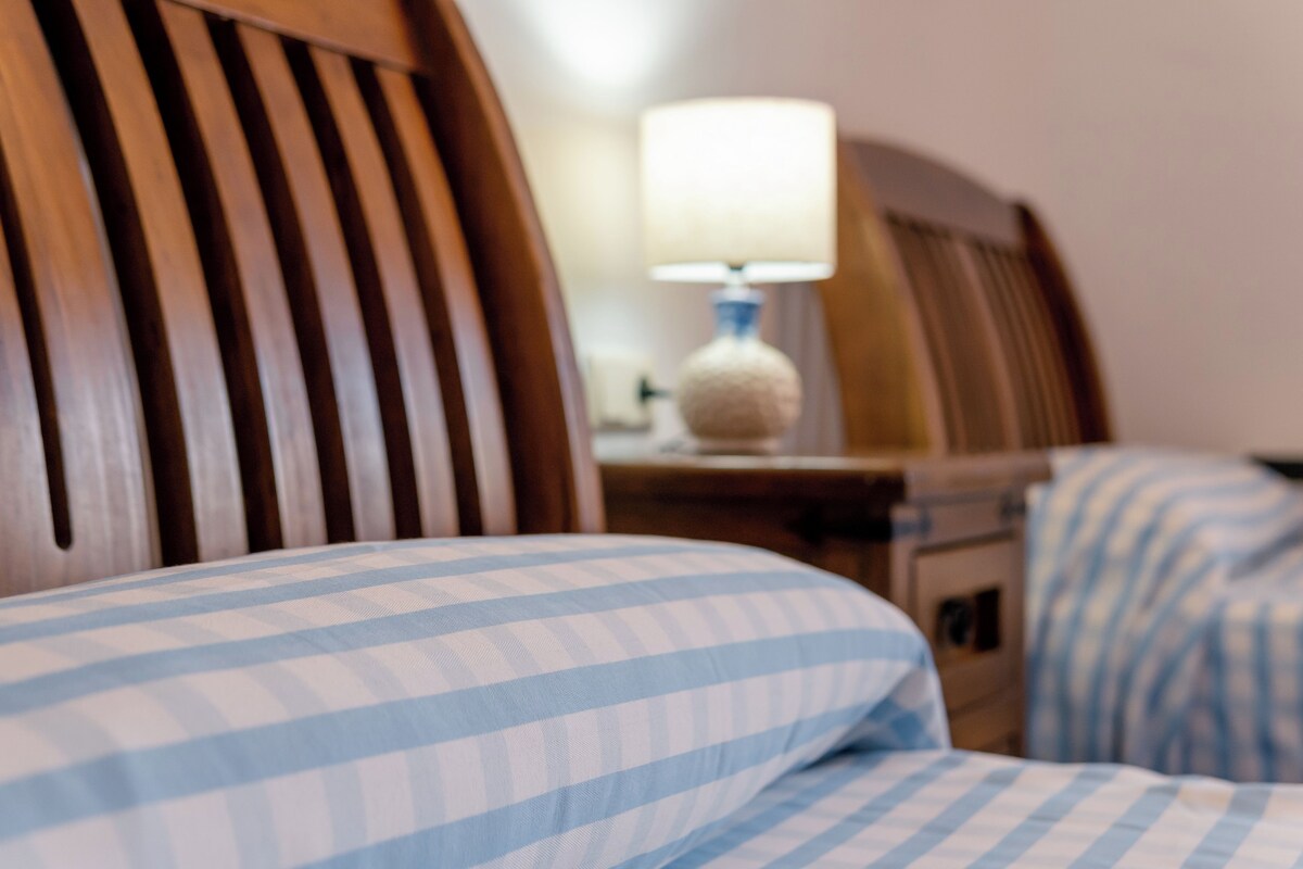Una habitación de hotel con cabecera de madera, una lámpara de noche y una colcha a cuadros.