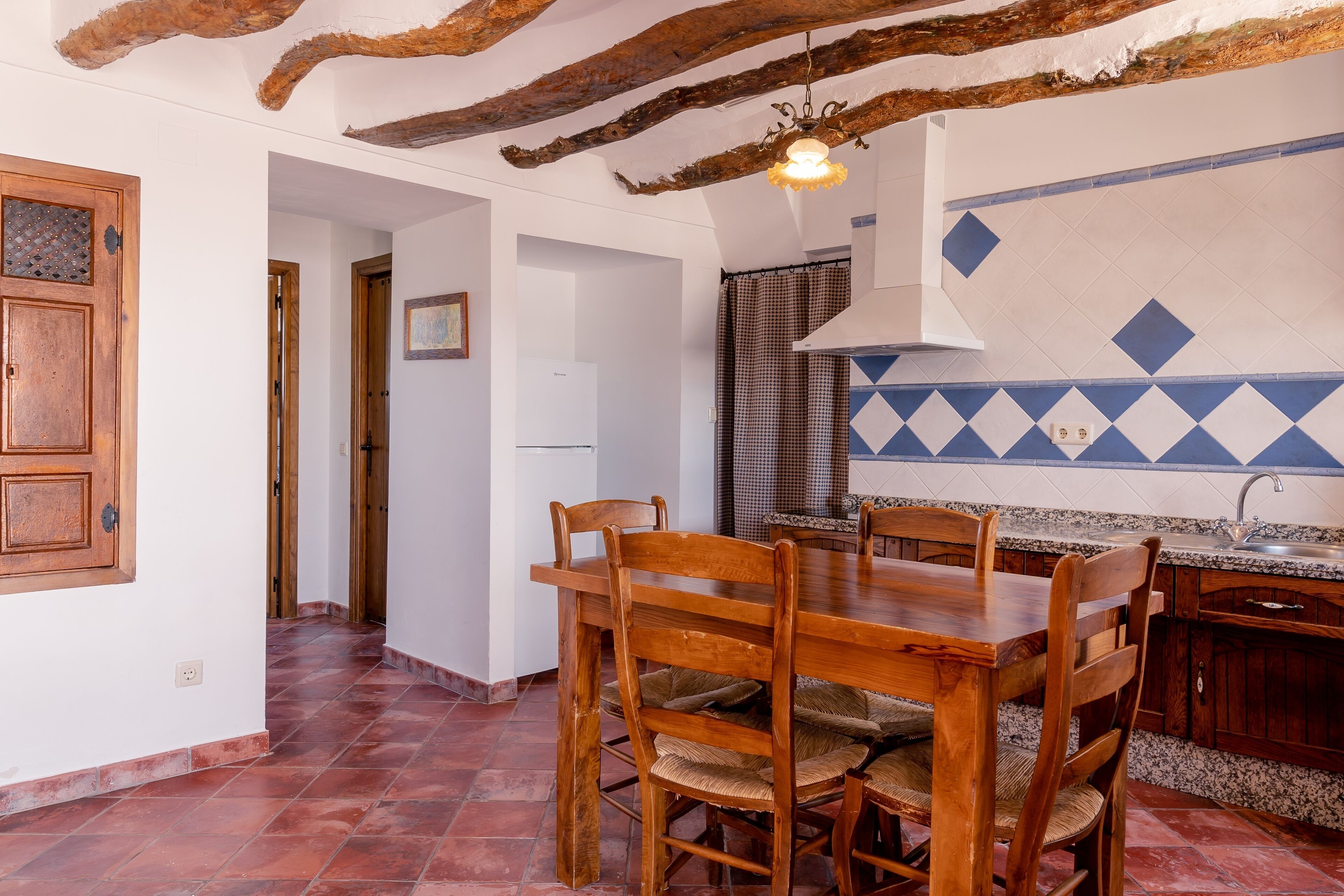 A kitchen with a wooden dining table, chairs, and a tiled backsplash.