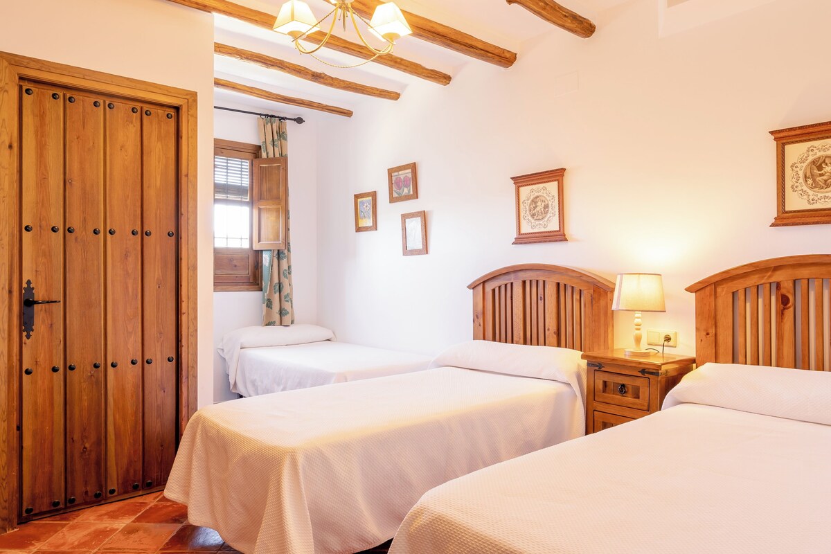 A hotel room with two beds, wooden headboards, a wooden wardrobe, and a nightstand with a lamp.