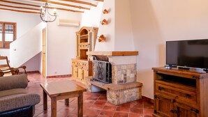 A living room with a stone fireplace, wooden furniture, and a television on a wooden stand. - Cortijo La Presa (Priego de Córdoba)