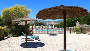 A poolside area with lounge chairs and thatched umbrellas, surrounded by greenery and a clear blue sky. - Cortijo La Presa (Priego de Córdoba)