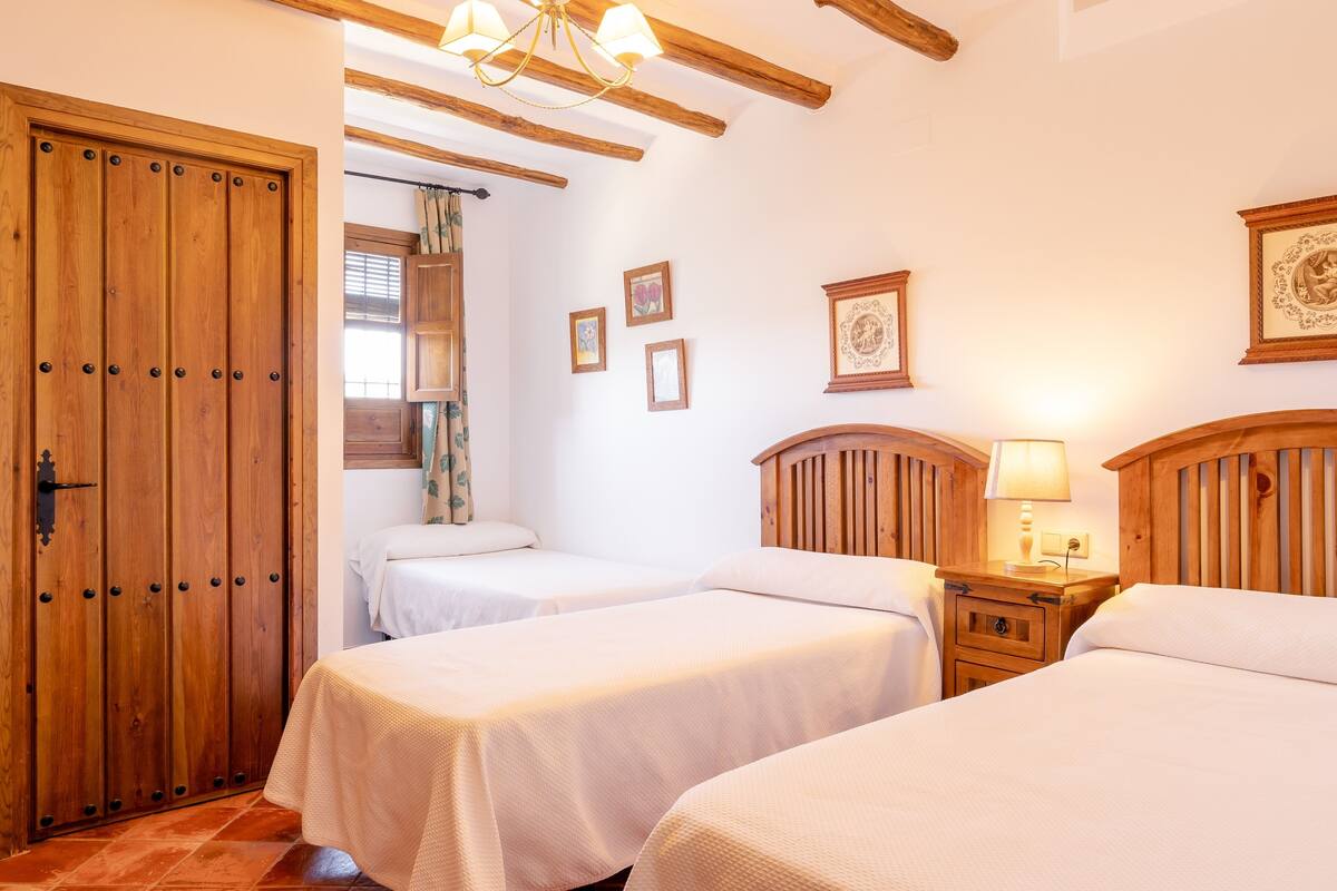 A hotel room with two beds, wooden headboards, a wooden wardrobe, and a nightstand with a lamp.