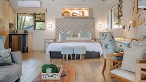 A bedroom with a thatched roof, a patterned headboard, a bed with pillows, a bedside table, and a chair. - La Roca Guest House (Mbombela)