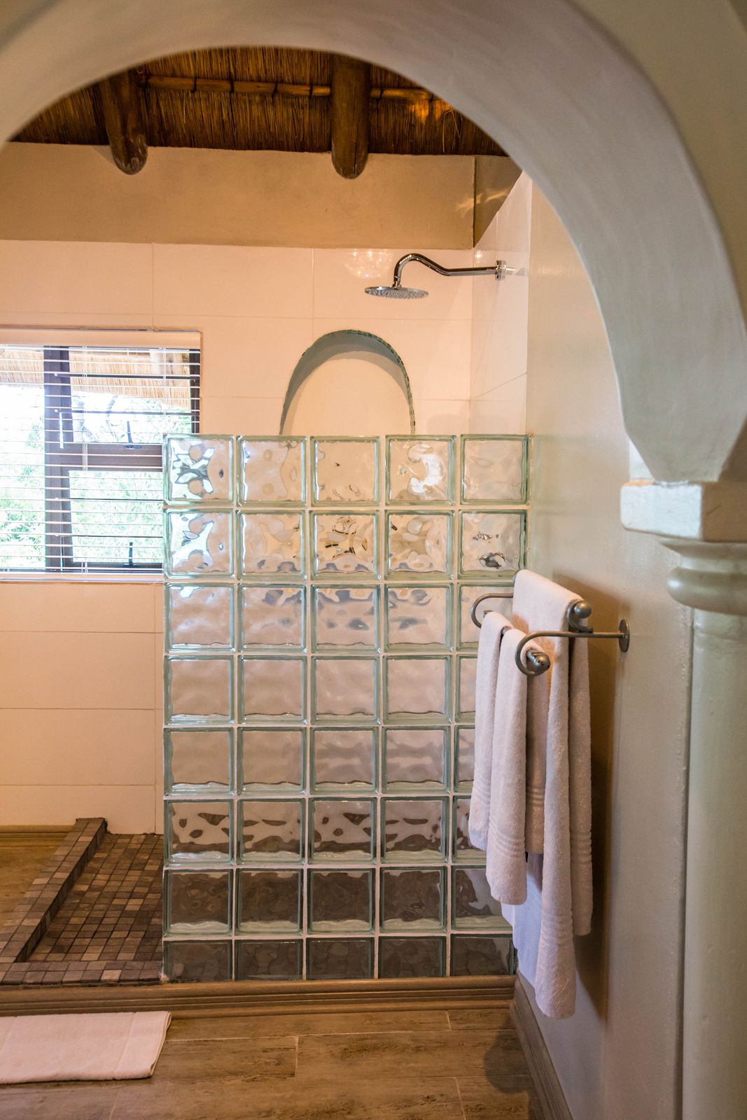 A shower with a glass block wall, a towel rack, and a window with blinds.