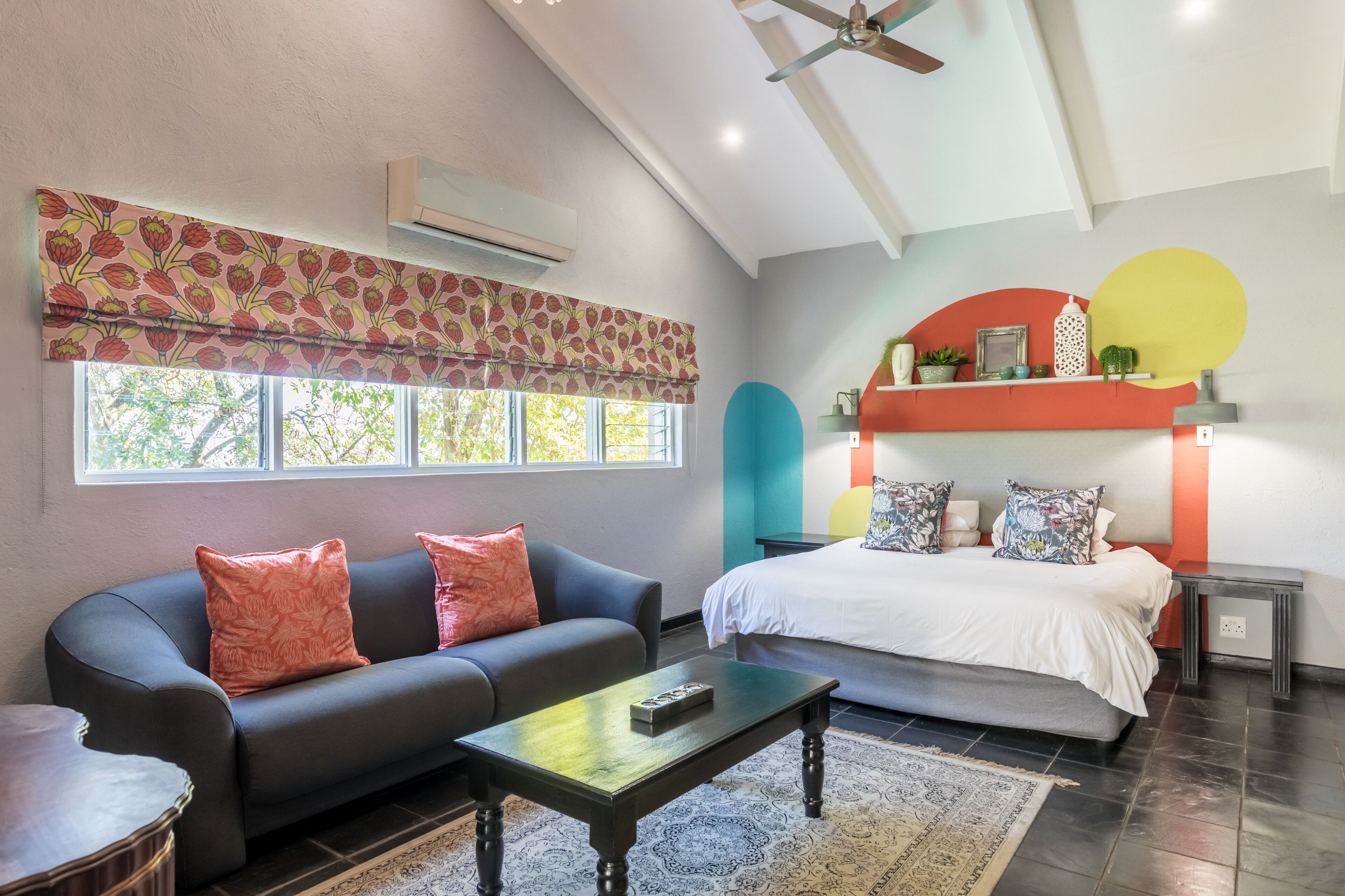 A modern bedroom with a bed, a sofa, a coffee table, and a window with a patterned curtain.