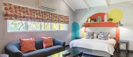 A modern bedroom with a bed, a sofa, a coffee table, and a window with a patterned curtain.