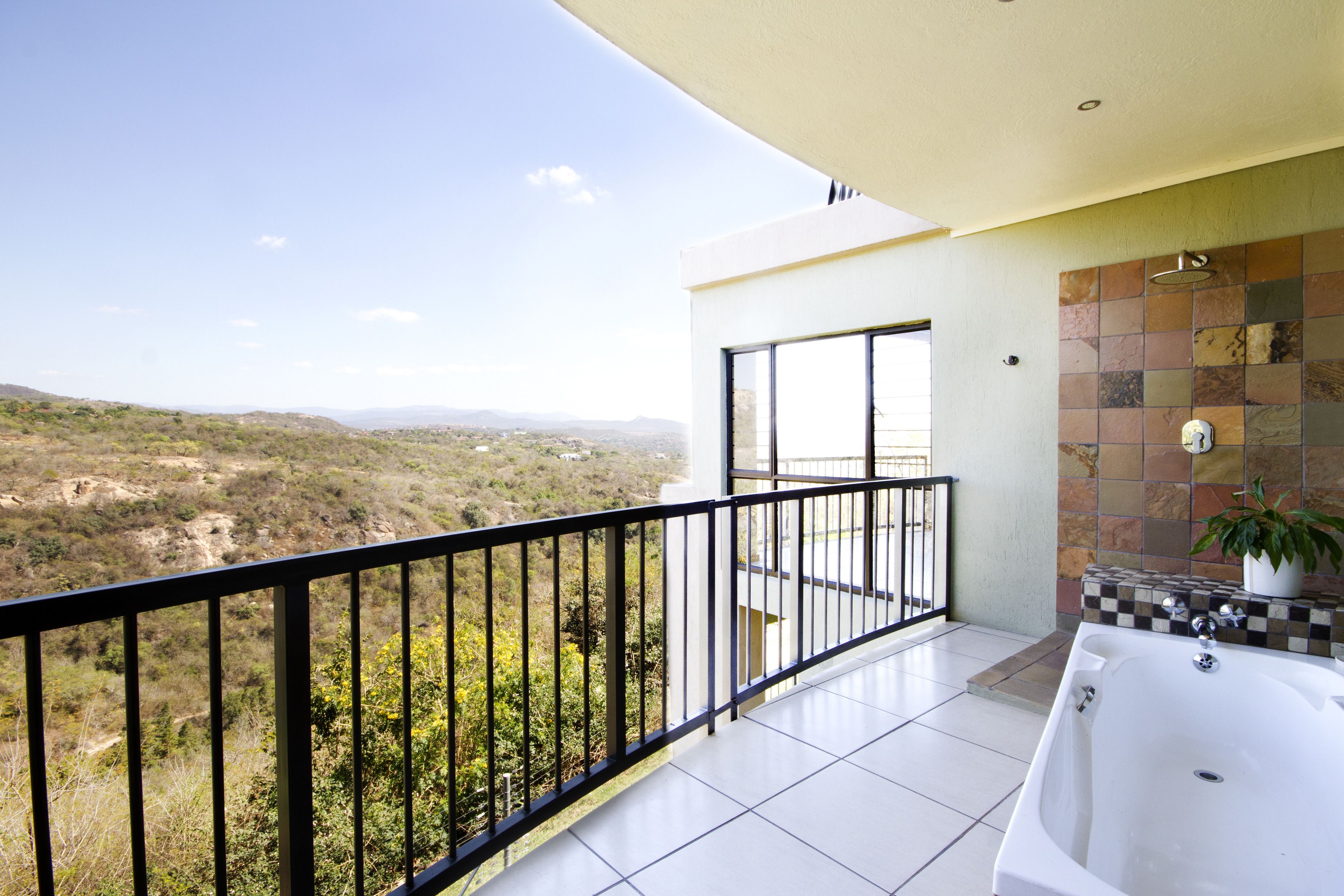 A balcony with a view of a hilly landscape, a bathtub, and a tiled wall.