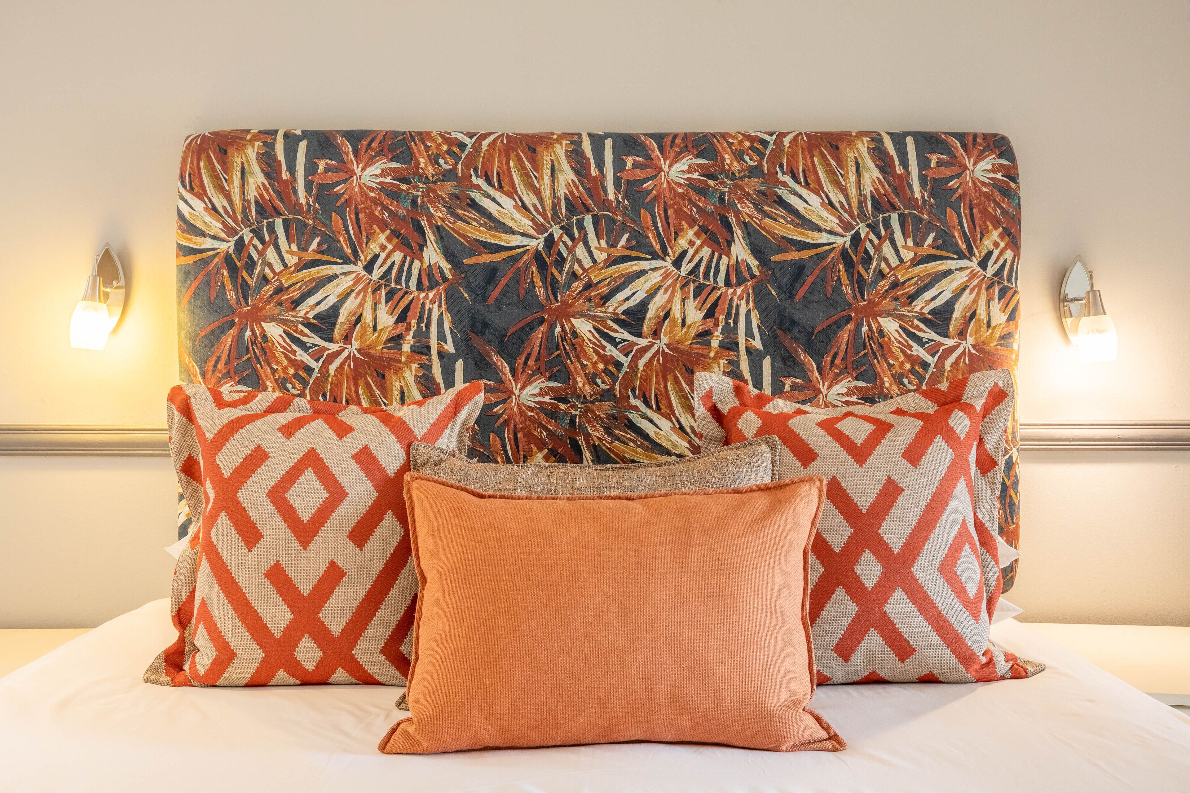 A bed with a patterned headboard, two wall-mounted lights, and multiple pillows.