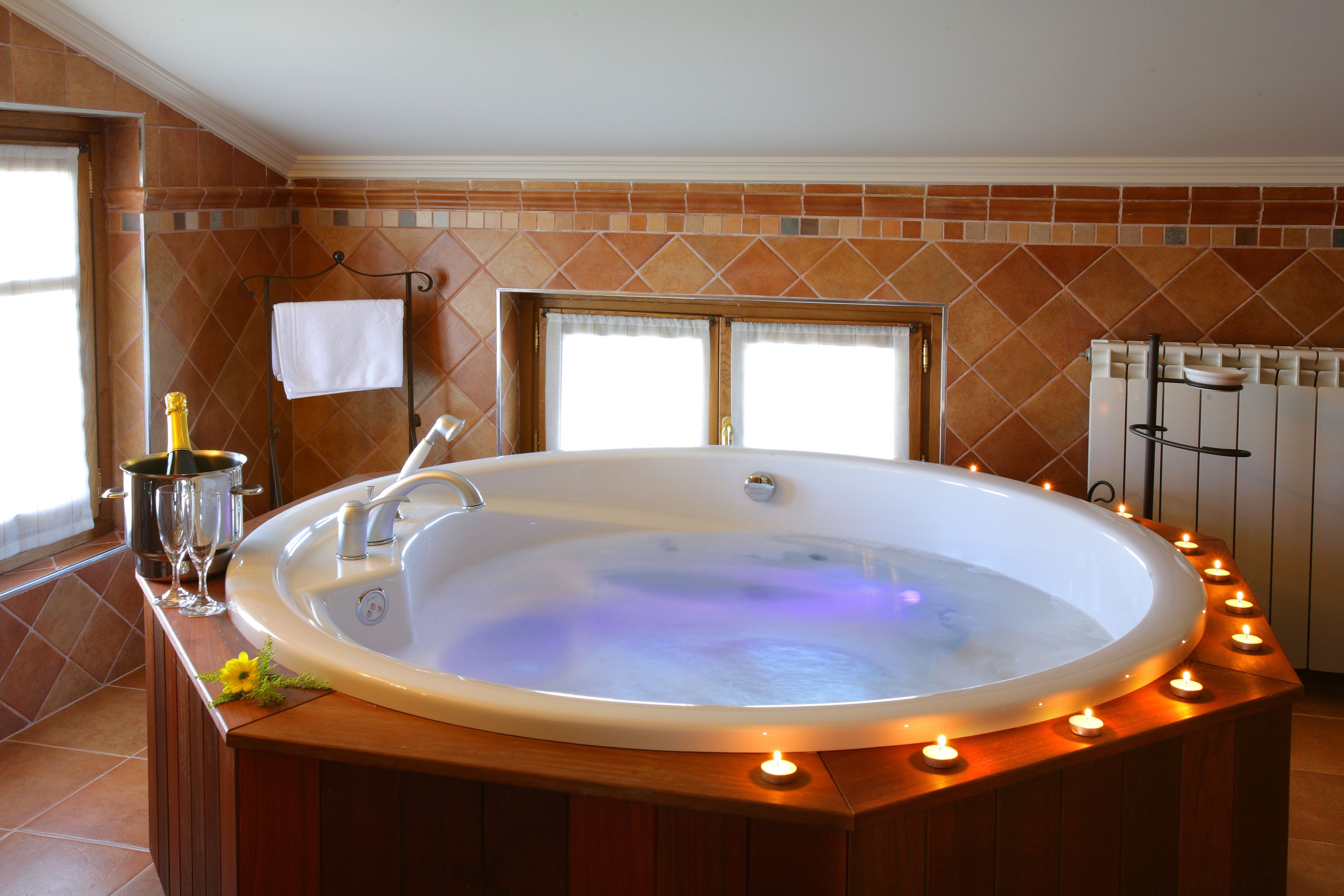 A hot tub with a wooden surround, a window with a towel, and a radiator.