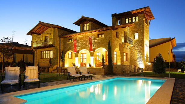 A stone building with a swimming pool, outdoor seating, and a well-lit entrance. - El Juglar (Olite)