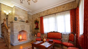 A traditional room with a stone fireplace, red upholstered chairs, and a wooden coffee table. - El Juglar (Olite)