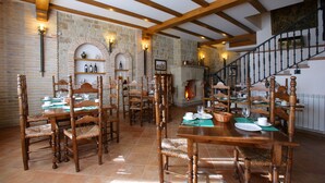 A dining area with wooden tables and chairs, stone walls, and a staircase. - El Juglar (Olite)