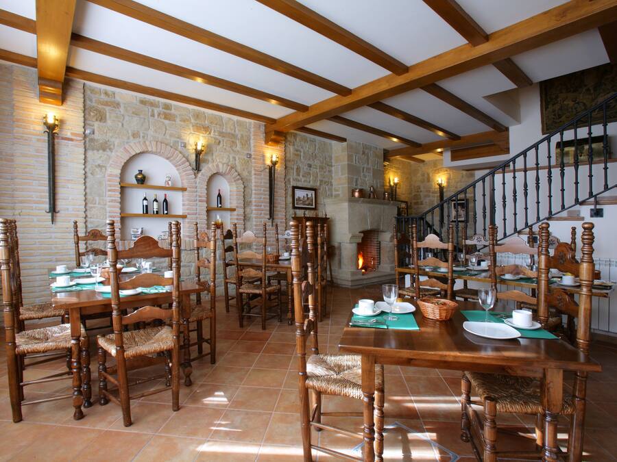 A dining area with wooden tables and chairs, stone walls, and a staircase.