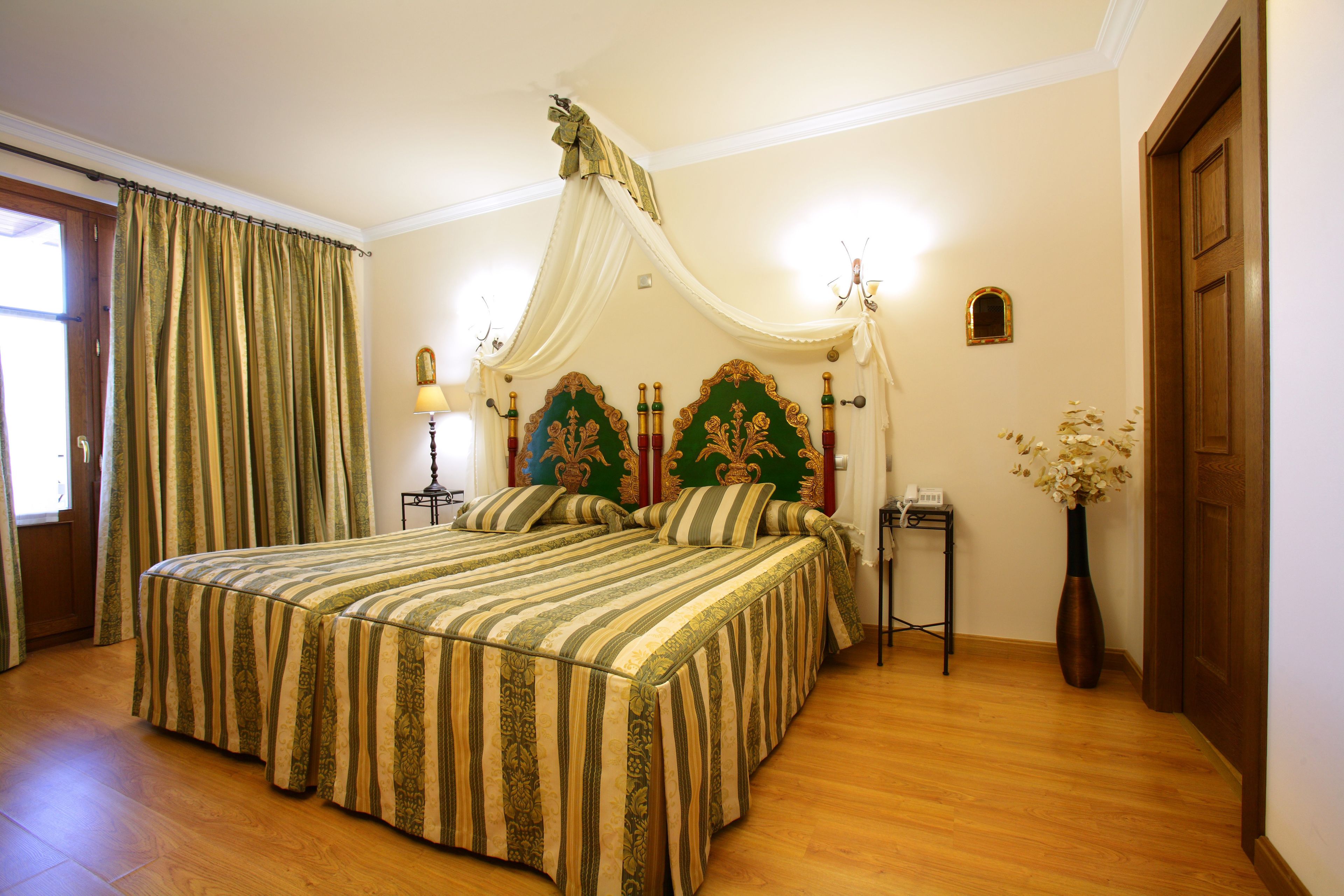 Un dormitorio con una cama grande, una mesita de noche, una lámpara, un florero con flores y una puerta.