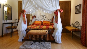 A four-poster canopy bed with a ruffled white canopy, a wooden floor, a small bench, and a chair. - El Juglar (Olite)