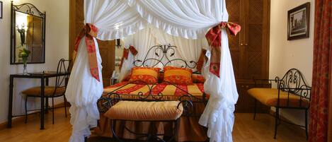 A four-poster canopy bed with a ruffled white canopy, a wooden floor, a small bench, and a chair.