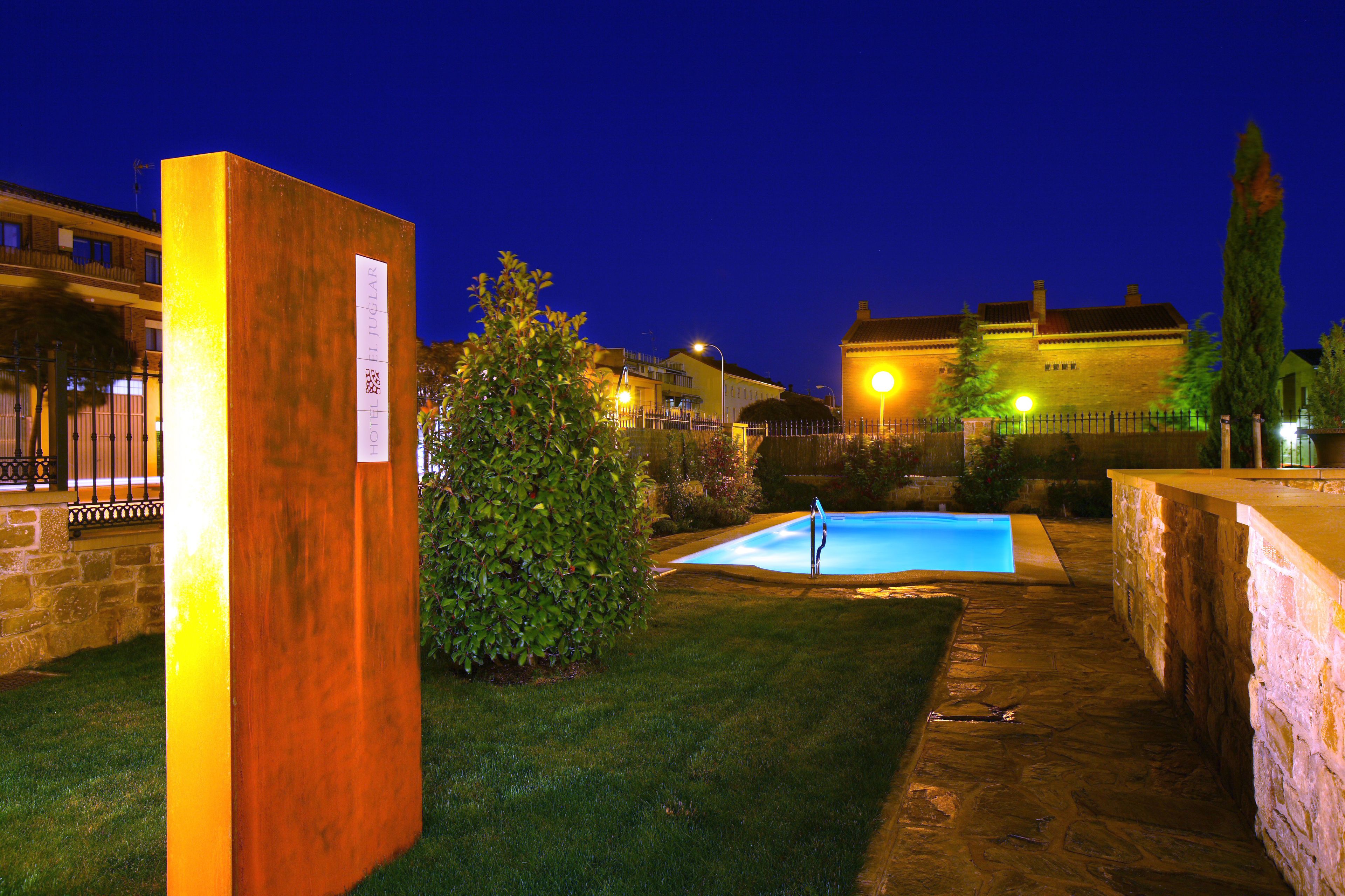 Un patio con piscina, una estructura de madera y un muro de piedra.