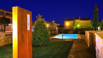 Un patio con piscina, una estructura de madera y un muro de piedra.