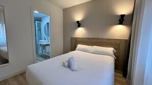 A neatly made bed with white linens and a rolled towel, a wooden headboard, and two wall-mounted lights. - IRAIPE GORBEA HOTEL (Vitoria-Gasteiz)