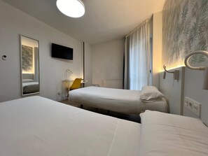 A hotel room with two beds, a television, a mirror, a desk with a chair, and a window with curtains. - IRAIPE GORBEA HOTEL (Vitoria-Gasteiz)