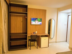 Een hotelkamer met een houten garderobe, een klein bureau met een stoel, een aan de muur bevestigde televisie en een spiegel.