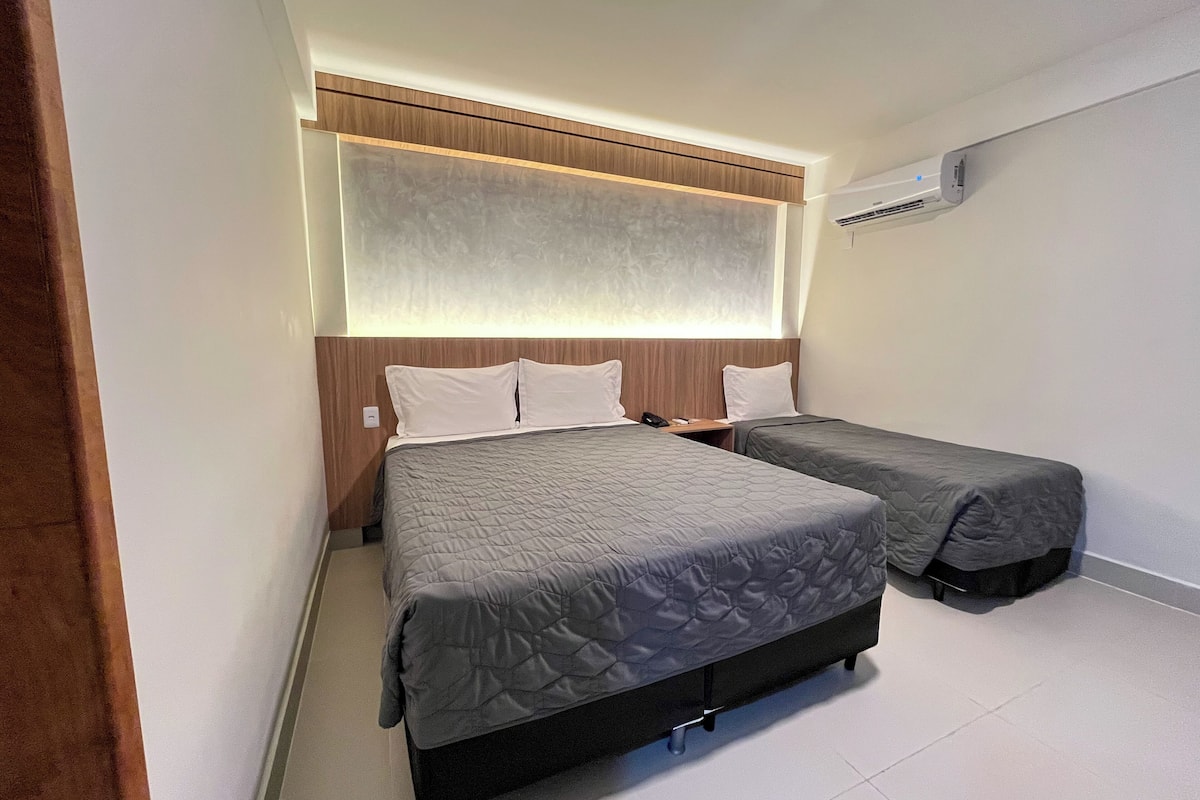 A hotel room with two beds, a wooden headboard, a wall-mounted air conditioner, and a white tiled floor.