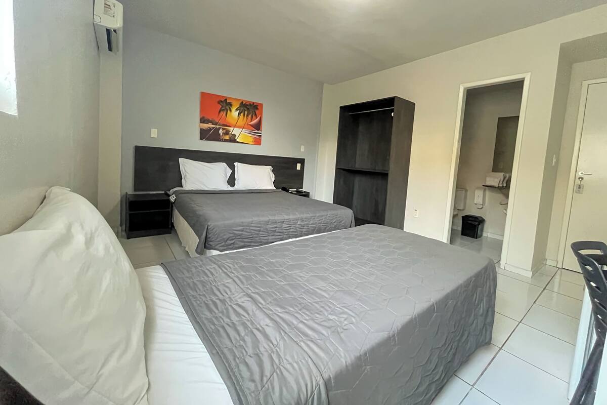A bedroom with two beds, a nightstand, a wardrobe, and a painting on the wall.
